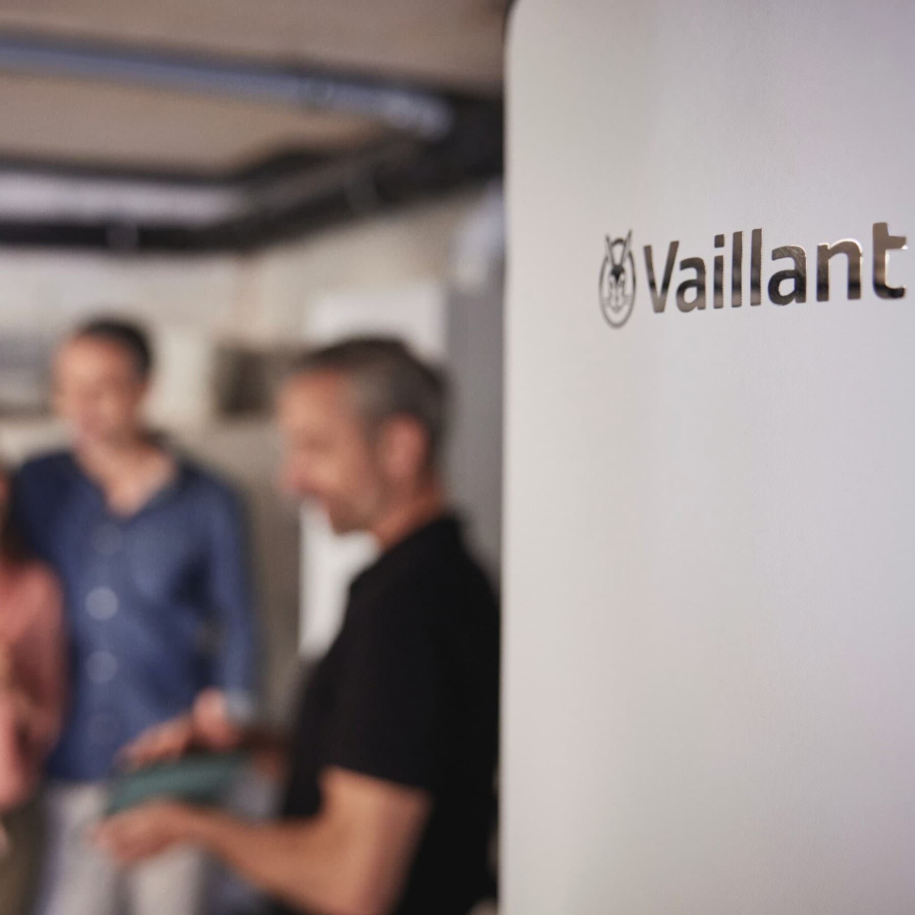 Un installateur expliquant le fonctionnement d'une chaudière à un client, debout dans la cuisine | Vaillant
