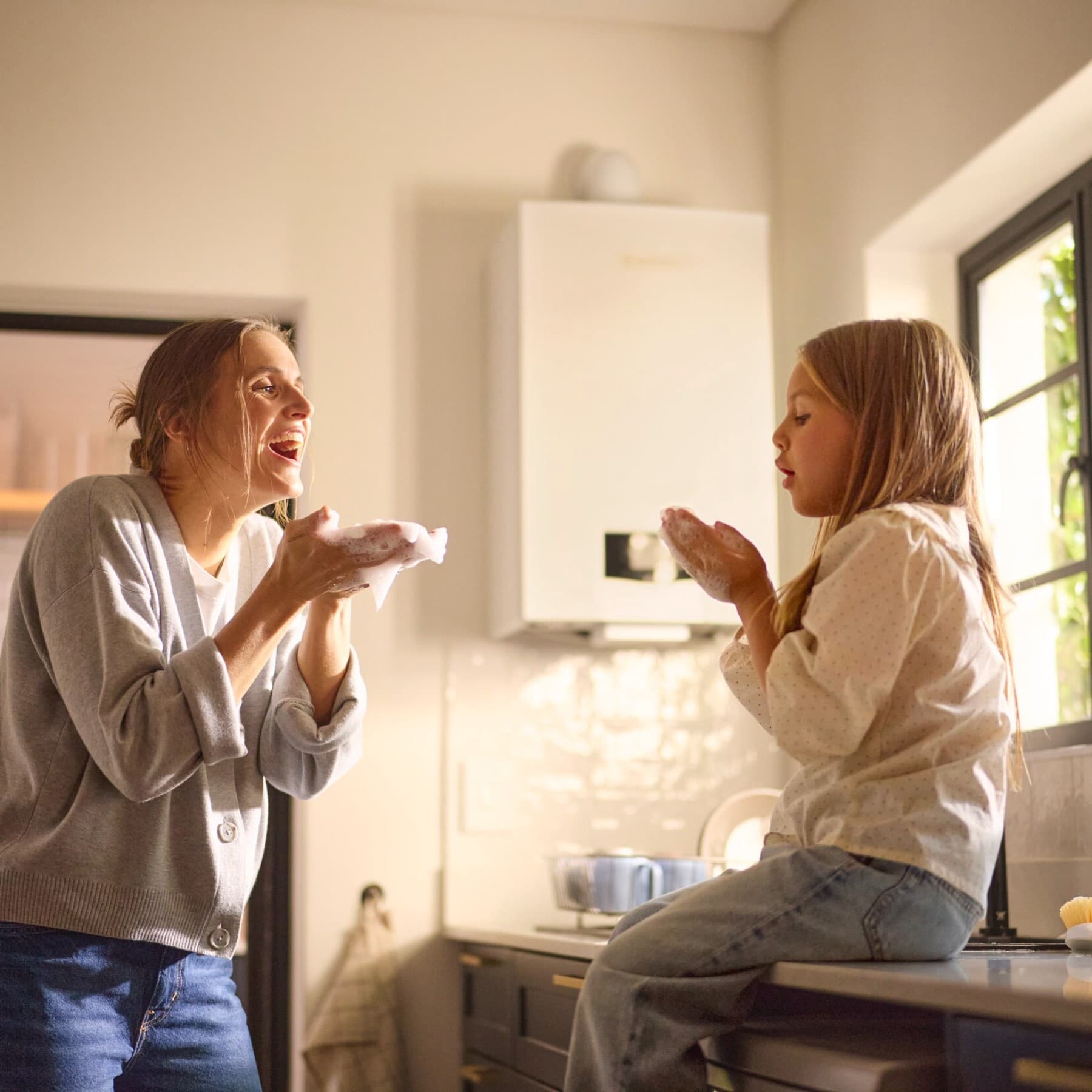 Une mère et sa fille jouent avec de la mousse de savon dans la cuisine | Vaillant