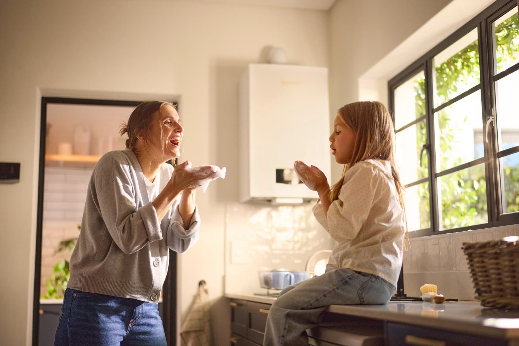 Une mère et sa fille jouant avec des bulles de savon avec une chaudière gaz dans le fond | Vaillant