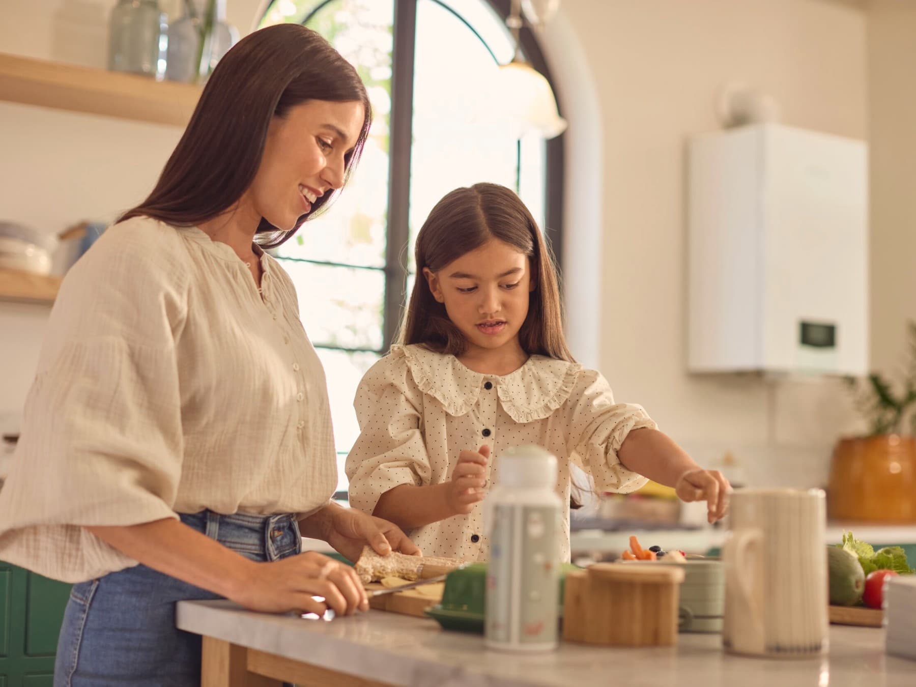 Une mère et sa fille font la cuisine avec en arrière plan une chaudière gaz et son conduit d'évacuation des fumées | Vaillant